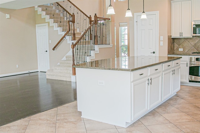 kitchen with appliances with stainless steel finishes, a center island, dark stone counters, and hanging light fixtures