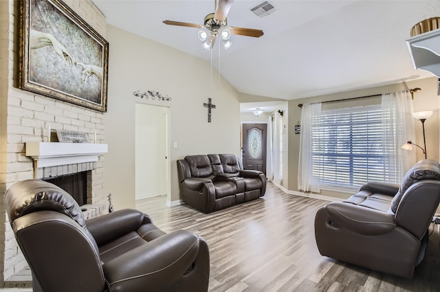 living room with vaulted ceiling, a brick fireplace, light hardwood / wood-style floors, and ceiling fan