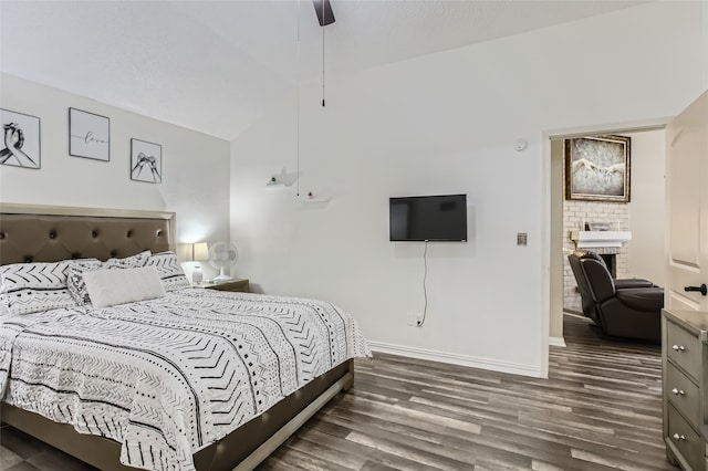 bedroom with ceiling fan, vaulted ceiling, a brick fireplace, and dark hardwood / wood-style flooring