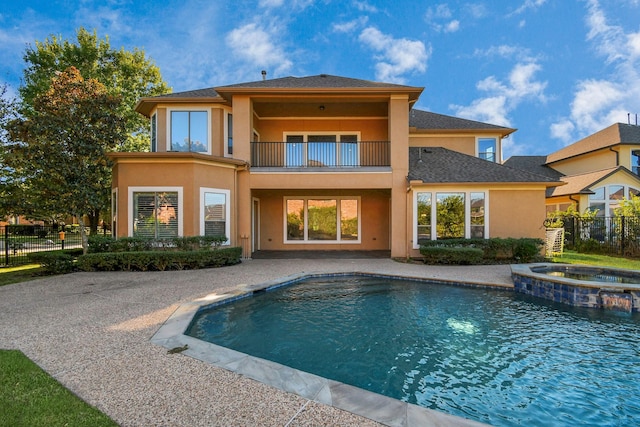 rear view of property with fence, a pool with connected hot tub, stucco siding, a patio area, and a balcony