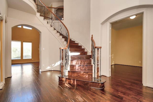 stairway with baseboards, arched walkways, a high ceiling, and wood finished floors