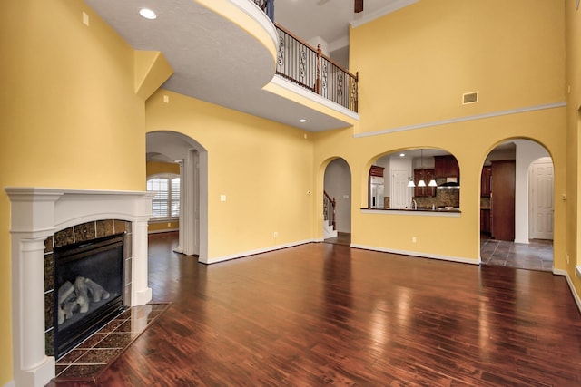 unfurnished living room featuring visible vents, a towering ceiling, wood finished floors, a fireplace, and baseboards