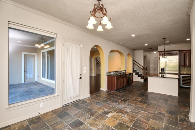 kitchen featuring stainless steel built in fridge, an island with sink, decorative light fixtures, and an inviting chandelier