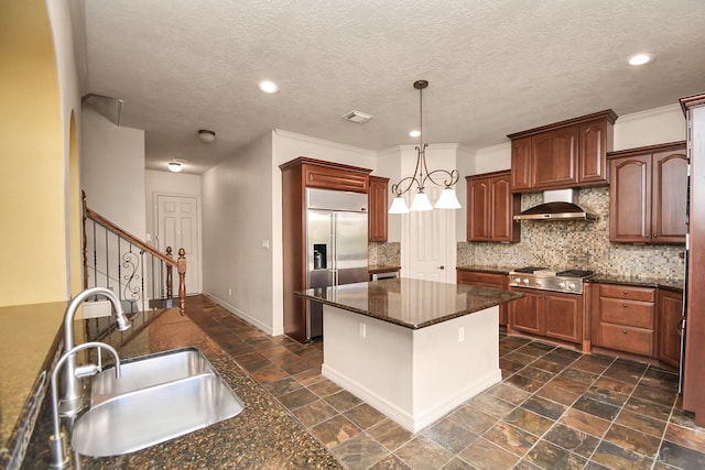 kitchen with wall chimney range hood, appliances with stainless steel finishes, tasteful backsplash, a sink, and stone tile floors