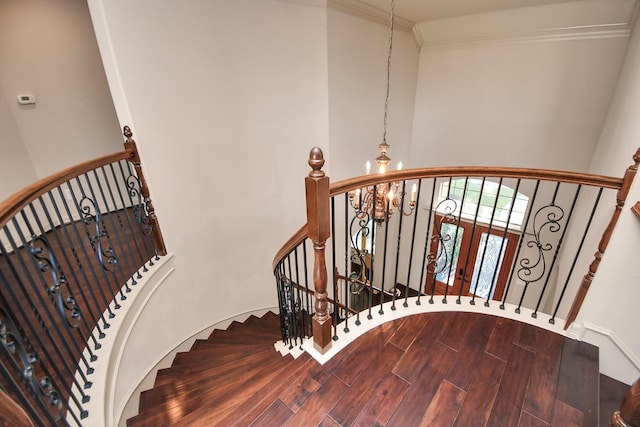 staircase featuring wood finished floors, ornamental molding, and a high ceiling