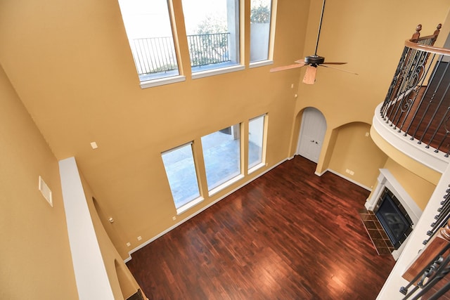 unfurnished living room featuring a tiled fireplace, a high ceiling, a ceiling fan, and wood finished floors