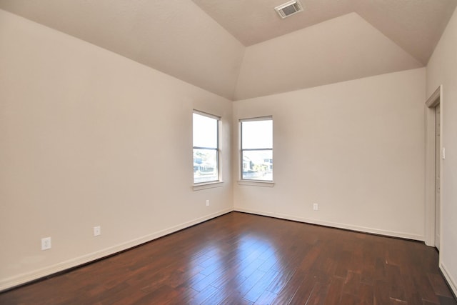 spare room featuring visible vents, dark wood-style flooring, baseboards, and vaulted ceiling