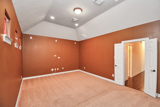 carpeted spare room featuring a textured ceiling and vaulted ceiling