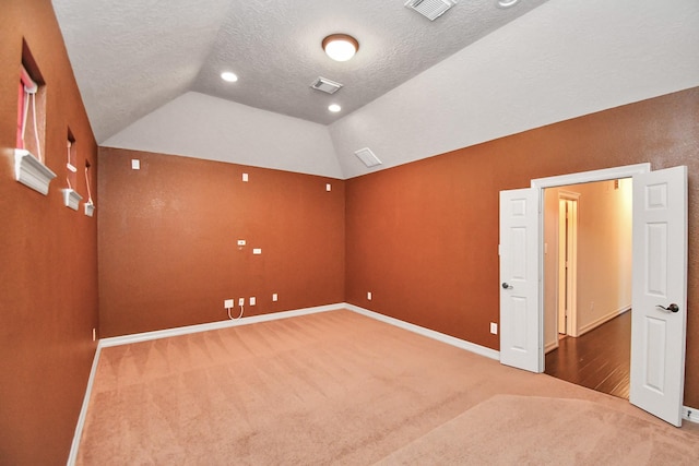 unfurnished room with visible vents, lofted ceiling, baseboards, a textured ceiling, and carpet