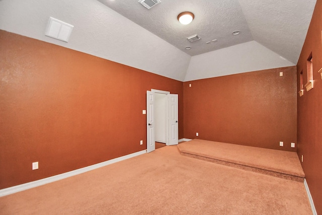 carpeted spare room featuring visible vents, baseboards, a textured ceiling, and lofted ceiling
