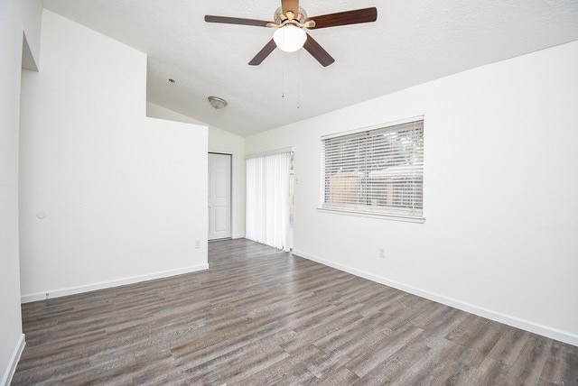 spare room featuring dark wood-type flooring, vaulted ceiling, a textured ceiling, and ceiling fan