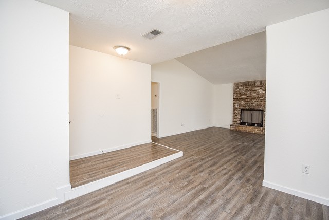 unfurnished living room with hardwood / wood-style floors, a textured ceiling, vaulted ceiling, and a brick fireplace