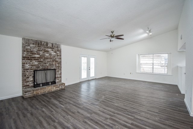 unfurnished living room featuring dark wood-type flooring, vaulted ceiling, a brick fireplace, and plenty of natural light