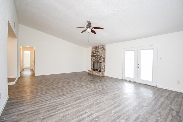 unfurnished living room featuring lofted ceiling, ceiling fan, wood-type flooring, a brick fireplace, and french doors