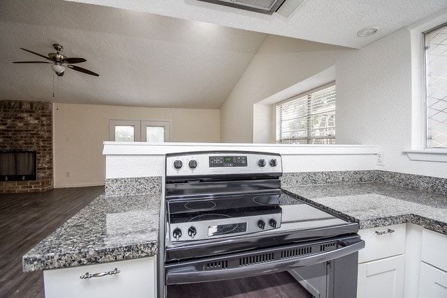 kitchen featuring lofted ceiling, dark wood-type flooring, kitchen peninsula, stainless steel range with electric cooktop, and white cabinets