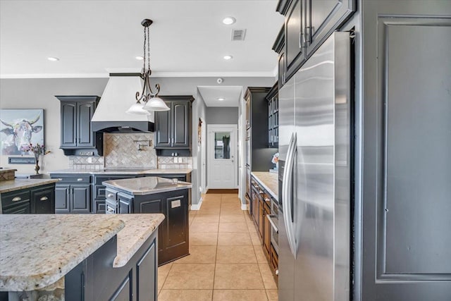 kitchen with stainless steel built in fridge, decorative backsplash, hanging light fixtures, premium range hood, and a center island