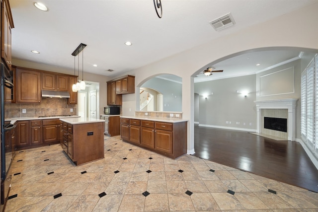 kitchen with hanging light fixtures, a kitchen island, stainless steel gas stovetop, light hardwood / wood-style flooring, and ornamental molding