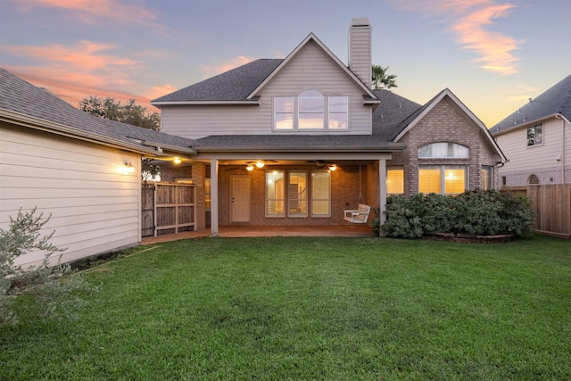 back house at dusk featuring a patio and a lawn