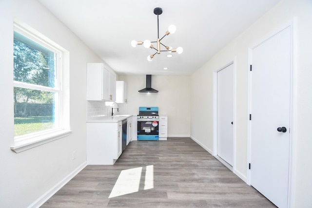 kitchen featuring wall chimney range hood, appliances with stainless steel finishes, a healthy amount of sunlight, white cabinets, and decorative backsplash