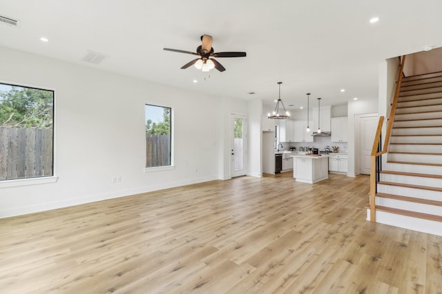 unfurnished living room with a healthy amount of sunlight, ceiling fan with notable chandelier, and light wood-type flooring