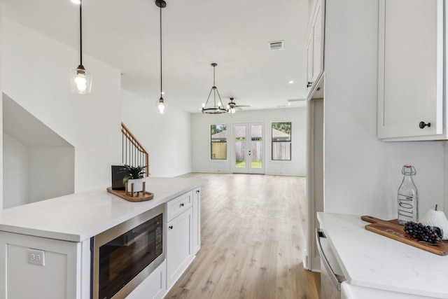 kitchen featuring white cabinetry, black microwave, hanging light fixtures, and light hardwood / wood-style floors