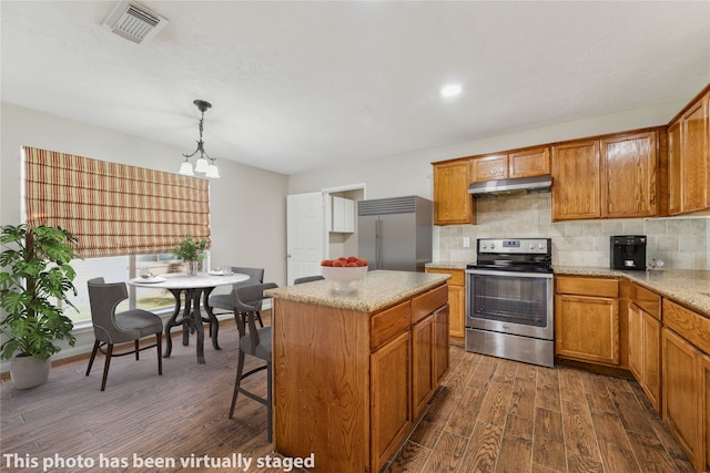 kitchen with appliances with stainless steel finishes, decorative light fixtures, dark hardwood / wood-style floors, decorative backsplash, and a center island