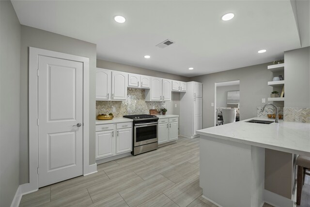 kitchen with white cabinetry, sink, kitchen peninsula, and stainless steel stove