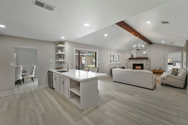 kitchen with kitchen peninsula, vaulted ceiling with beams, sink, a stone fireplace, and decorative light fixtures