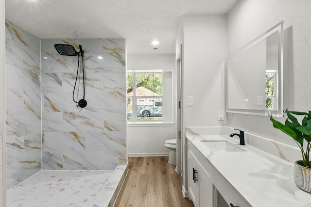 bathroom featuring toilet, hardwood / wood-style flooring, vanity, and a tile shower