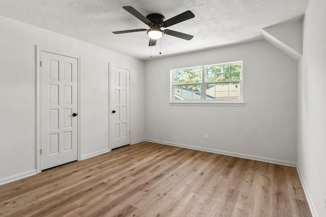 unfurnished bedroom featuring light wood-type flooring, a textured ceiling, ceiling fan, lofted ceiling, and two closets