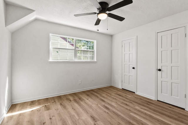 unfurnished bedroom with lofted ceiling, ceiling fan, a textured ceiling, multiple closets, and light hardwood / wood-style floors