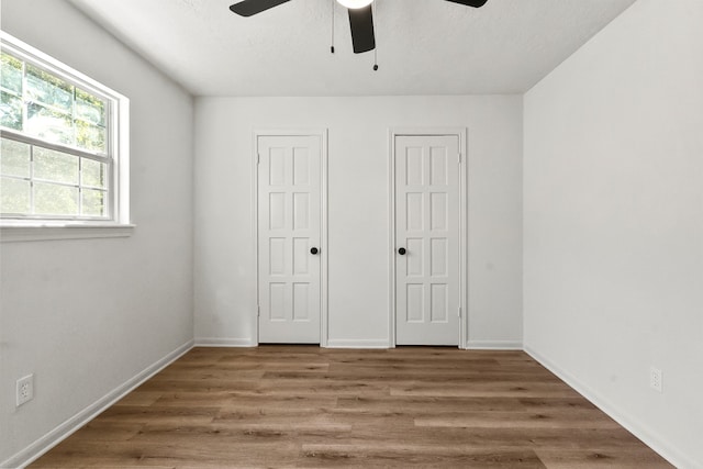 unfurnished bedroom with multiple closets, wood-type flooring, and ceiling fan