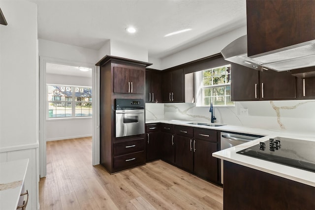 kitchen with appliances with stainless steel finishes, sink, dark brown cabinets, and light wood-type flooring