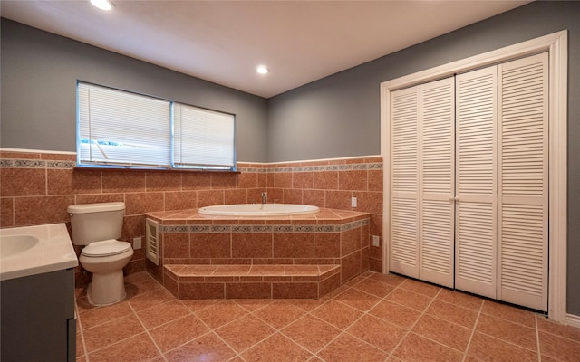 bathroom with tile patterned floors, toilet, tiled tub, vanity, and tile walls