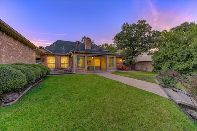 back house at dusk with a patio and a lawn