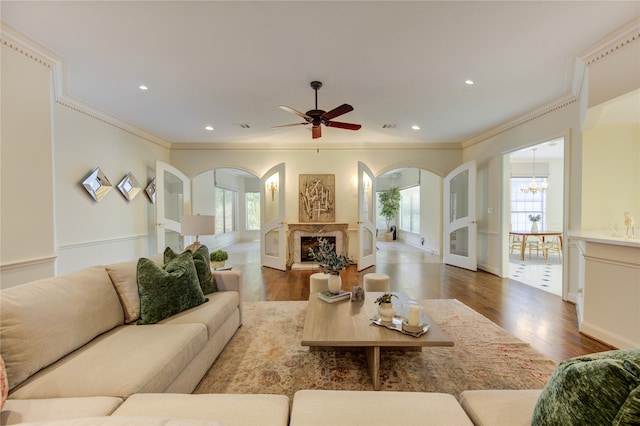 living room featuring wood-type flooring, ceiling fan with notable chandelier, and ornamental molding