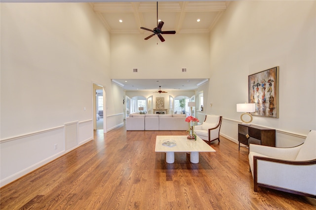 living room featuring ornamental molding, a towering ceiling, beam ceiling, coffered ceiling, and hardwood / wood-style flooring