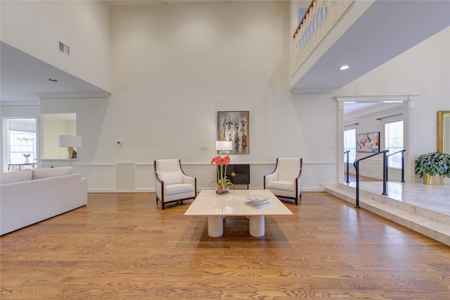 living area featuring a towering ceiling, light wood-type flooring, and crown molding