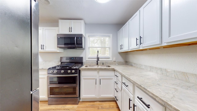 kitchen with white cabinets, light stone counters, appliances with stainless steel finishes, light hardwood / wood-style flooring, and sink