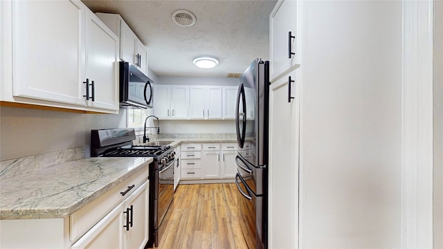 kitchen featuring light hardwood / wood-style flooring, black appliances, sink, white cabinetry, and light stone counters