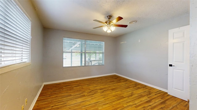 empty room with a wealth of natural light, hardwood / wood-style floors, a textured ceiling, and ceiling fan