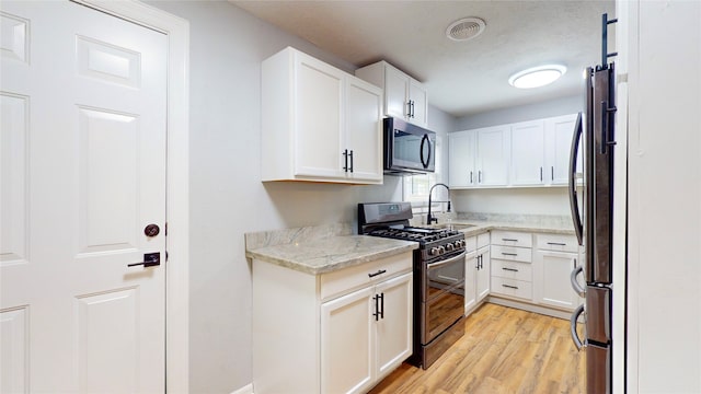 kitchen with light stone countertops, white cabinets, stainless steel appliances, and light hardwood / wood-style floors