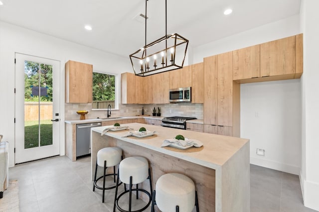 kitchen featuring tasteful backsplash, light countertops, appliances with stainless steel finishes, a kitchen island, and a sink