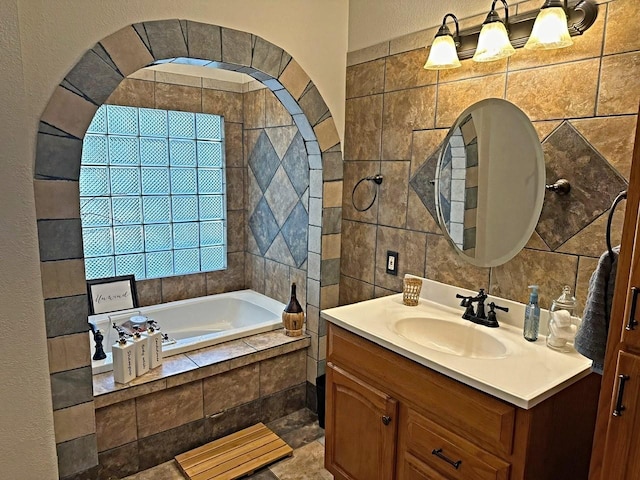 bathroom featuring vanity, a relaxing tiled tub, and tile walls