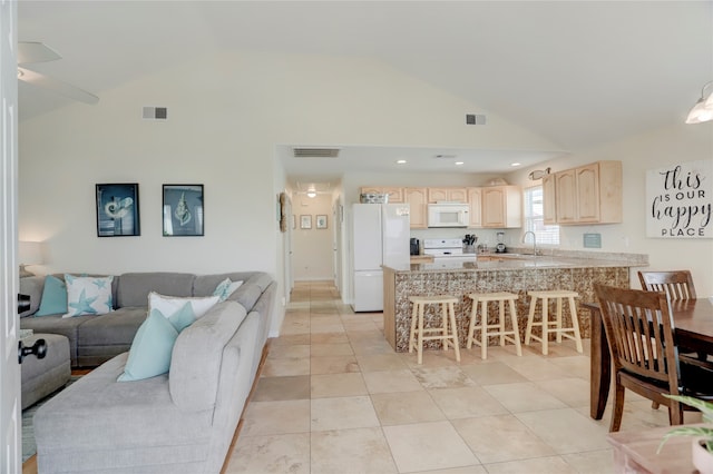 interior space featuring light brown cabinets, sink, kitchen peninsula, white appliances, and a kitchen bar