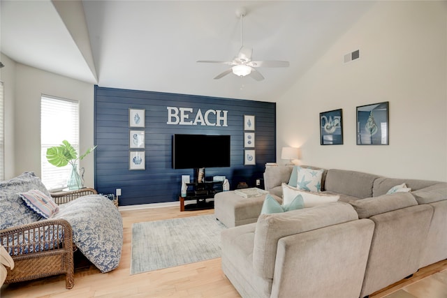 living room with high vaulted ceiling, light hardwood / wood-style flooring, ceiling fan, and wooden walls