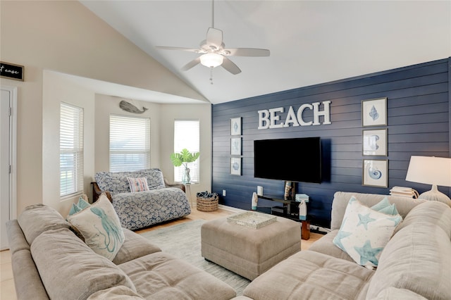 living room featuring high vaulted ceiling, ceiling fan, light hardwood / wood-style floors, and wooden walls