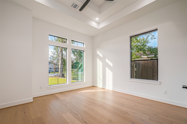 spare room with a raised ceiling, a high ceiling, light wood-type flooring, and ceiling fan