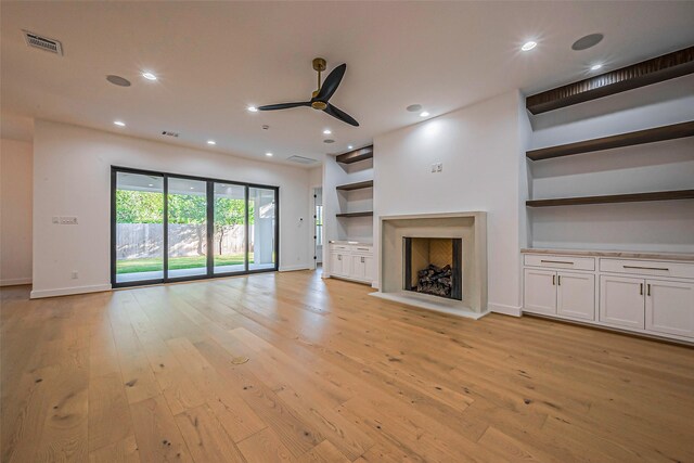 unfurnished living room featuring ceiling fan, a fireplace, built in features, light wood-type flooring, and visible vents