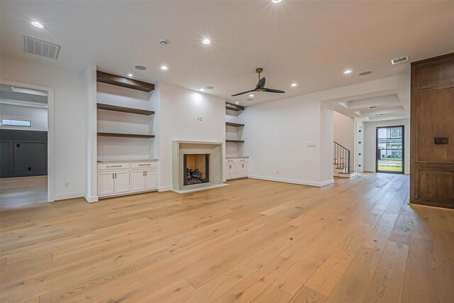 unfurnished living room featuring ceiling fan, visible vents, built in features, light wood-type flooring, and stairs